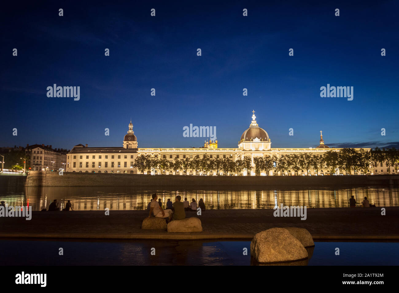 LYON, Frankreich - 18. JULI 2019: Franzosen sitzen am Ufer des Quais de Rhone, gegenüber Hotel Dieu, eines der wichtigsten Denkmäler der Stadt w Stockfoto