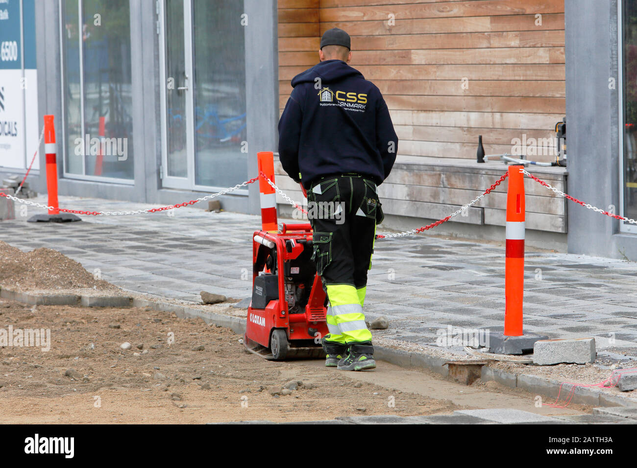 Kopenhagen, Dänemark - 4. September 2019.: Rückansicht eines männlichen Arbeitnehmers mit einer roten Rüttelplatte verdichten Kies zu einem Straßenbau si Stockfoto