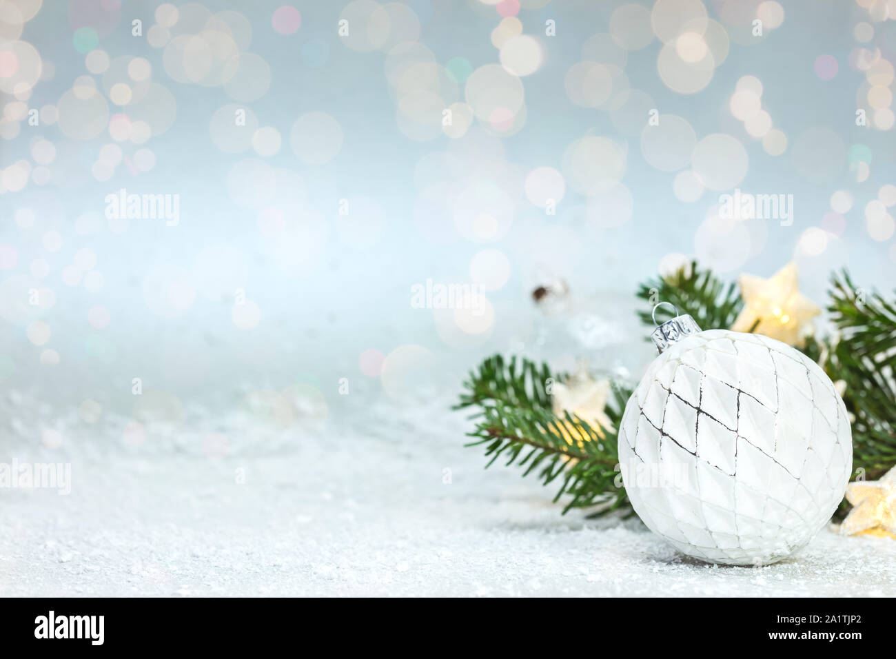 Schöne Weihnachten verschneite Hintergrund mit grünen Fir Tree Branch, weißem Glas Kugel und leuchtende Sterne leuchten Stockfoto