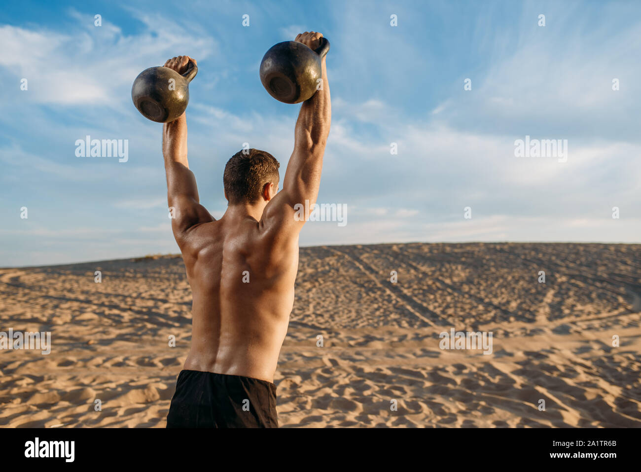 Männliche Athlet mit zwei Kettlebells in der Wüste Stockfoto