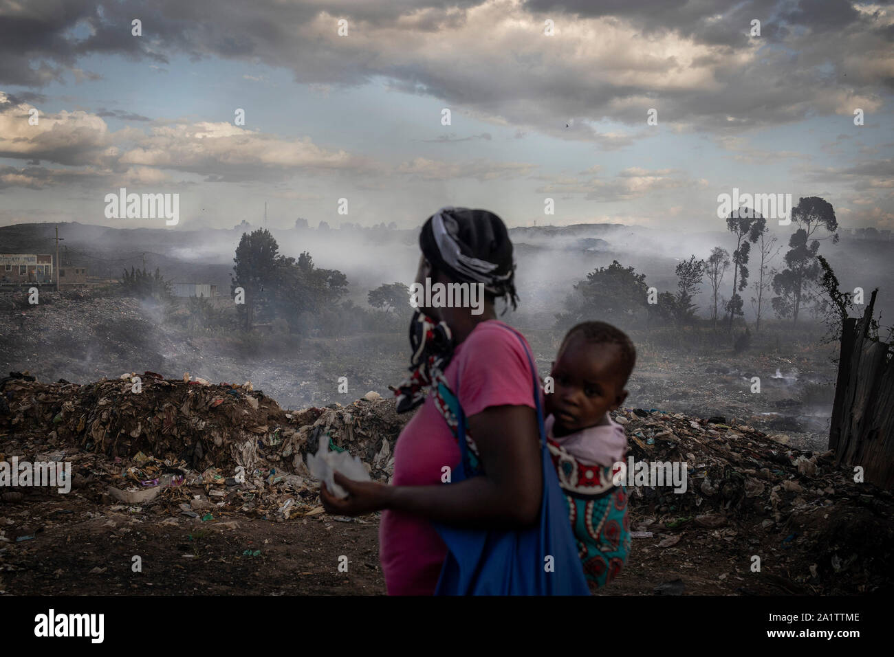 Eine Frau ihr Baby Mädchen tragen schaut die Dandora Deponie, am Rande der Elendsviertel von Korogocho in der Hauptstadt Nairobi, Kenia. Stockfoto