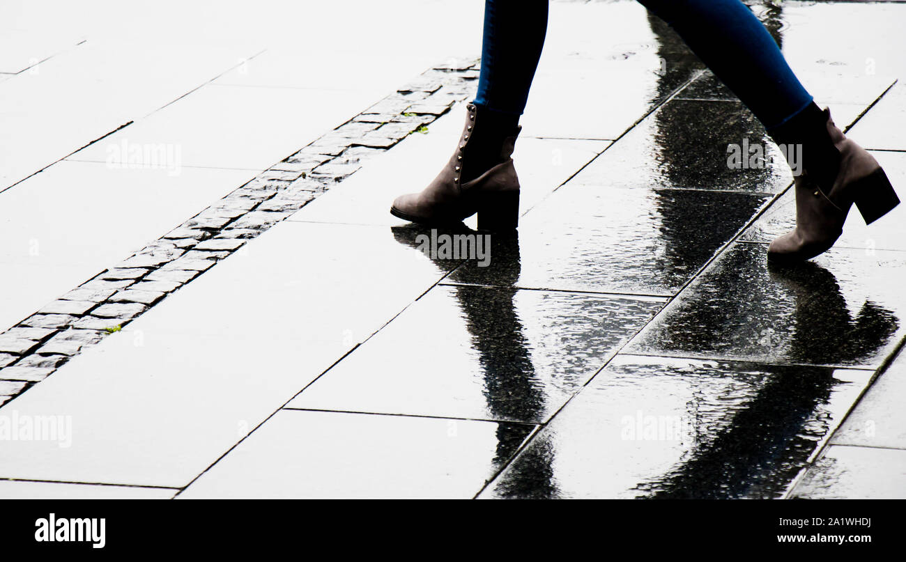 Silhouette Schatten und Reflexion einer Frau in Stiefelette Schuhe Wandern nasse Straße der Stadt an einem regnerischen Tag, Beine nur Stockfoto