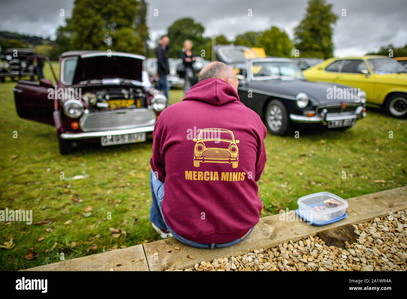 Ein Mann in einem Hoodie isst Mittag neben seinem Mini classic car Versammlung in Sudeley Castle, Cotswolds, wo mehrere Oldtimerbesitzer das Wetter ihre Fahrzeuge zu zeigen getrotzt haben. Stockfoto