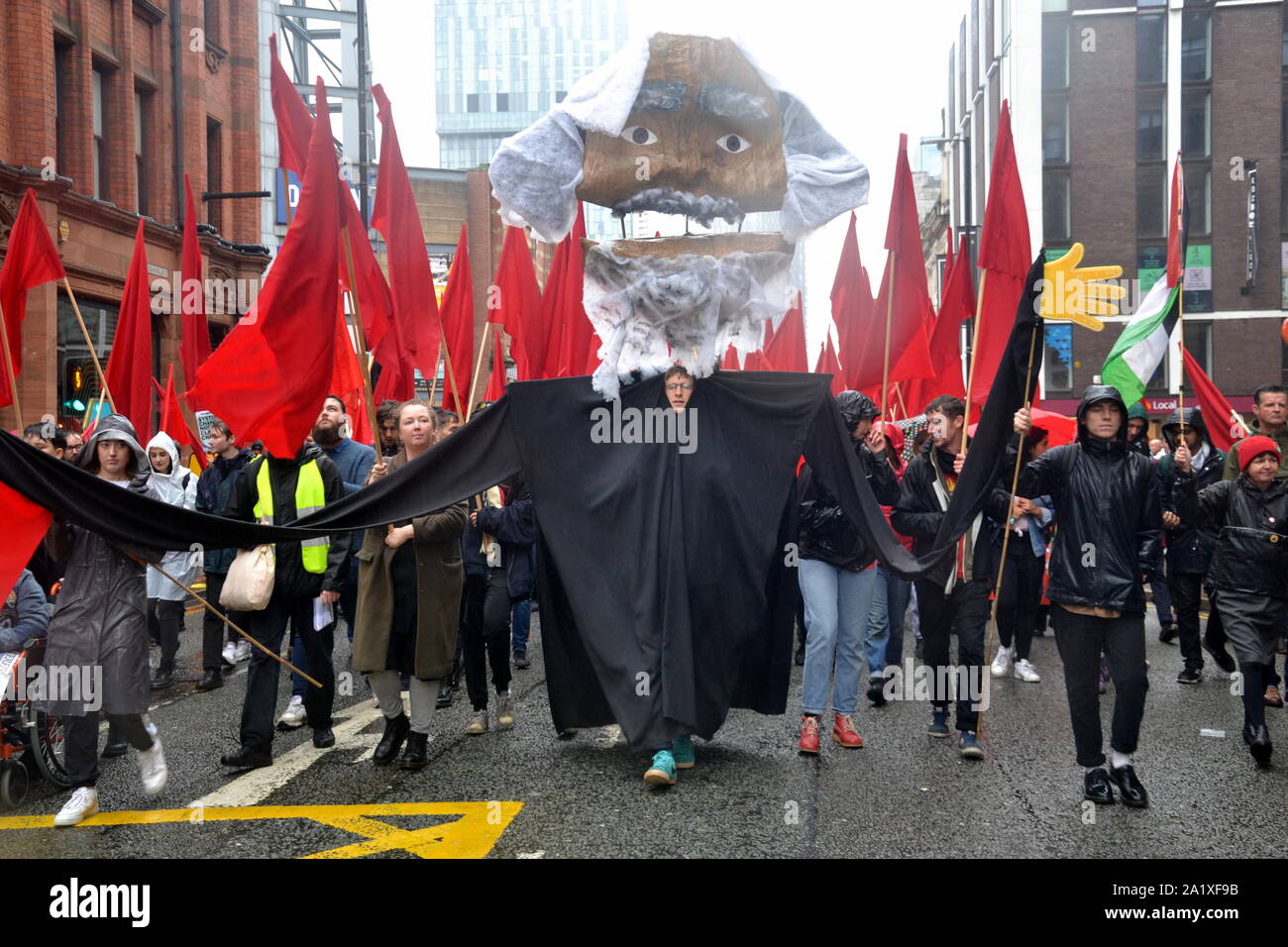 Die Volksversammlung gegen Sparpolitik organisiert eine große Protestmarsch durch die Innenstadt von Manchester, UK, zu Beginn der Konservativen Partei Konferenz 2019. Hier eine große Abbildung von Karl Marx führt eine Gruppe mit roten Fahnen. Stockfoto