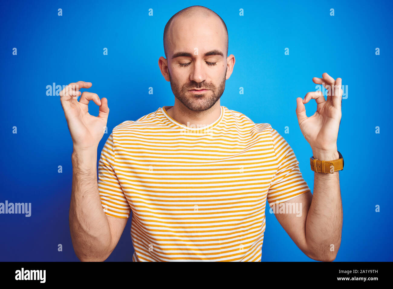 Junge glatzköpfige Mann mit Bart tragen casual t-shirt über Blau isoliert Hintergrund entspannen und Lächeln, mit geschlossenen Augen die Meditation Geste mit Finger Stockfoto