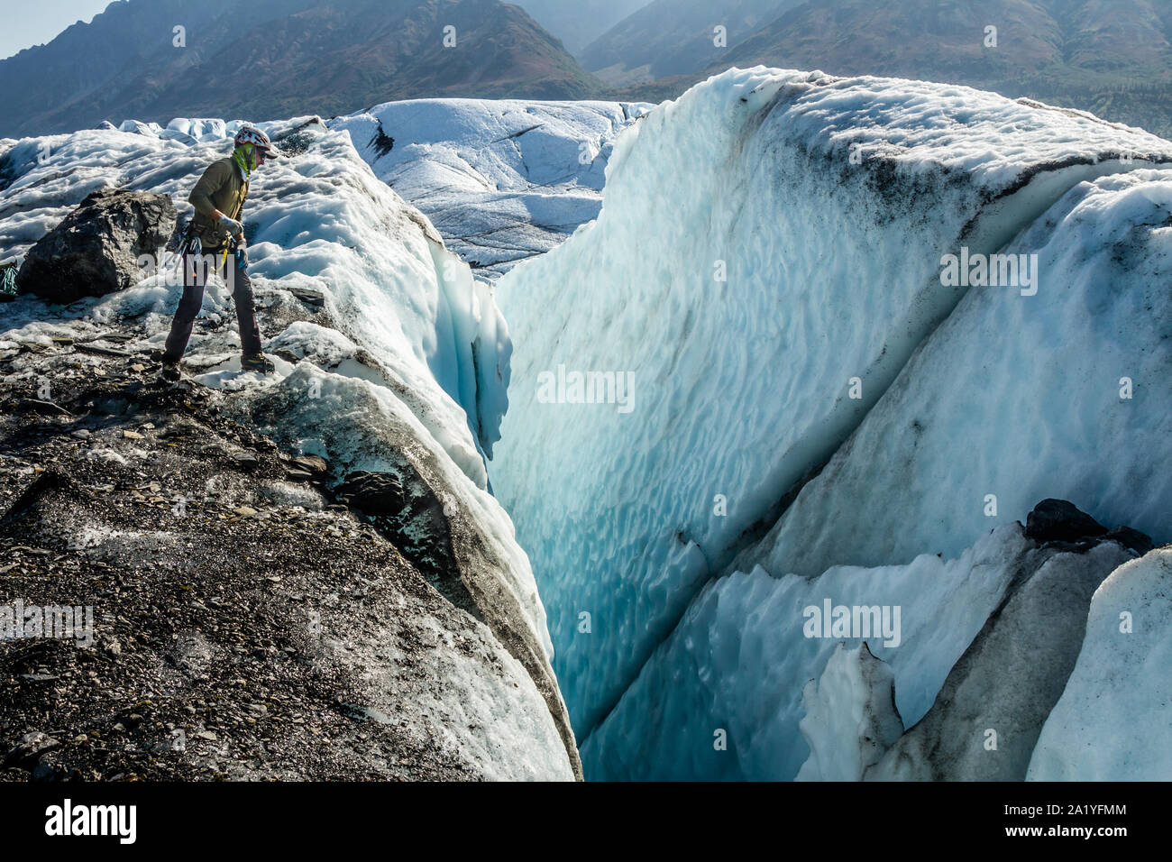Ice climber, schiefen Blicken in eine massive Gletscherspalte, suchen einen Ort, an einem Seil zu senken und in die Gletscherspalte. Stockfoto