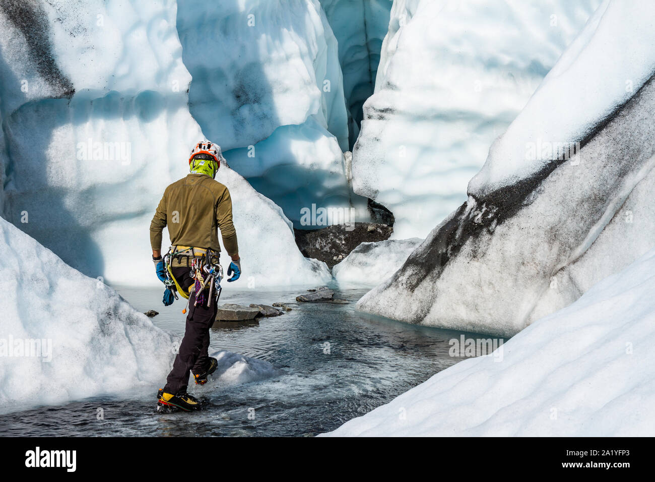 Eine junge eiskletterer Spaziergänge durch seichtes Wasser in Richtung einer großen Eishöhle auf der Matanuska Gletscher in Alaska. Stockfoto