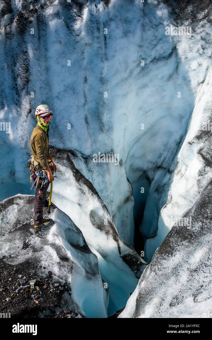 Ein junger Mann steht neben ein tiefes dunkles Loch auf der Matanuska Gletscher in Alaska. Er ist Scoping out ein guter Platz für ein Seil, so dass er sich in die dunkle h Stockfoto