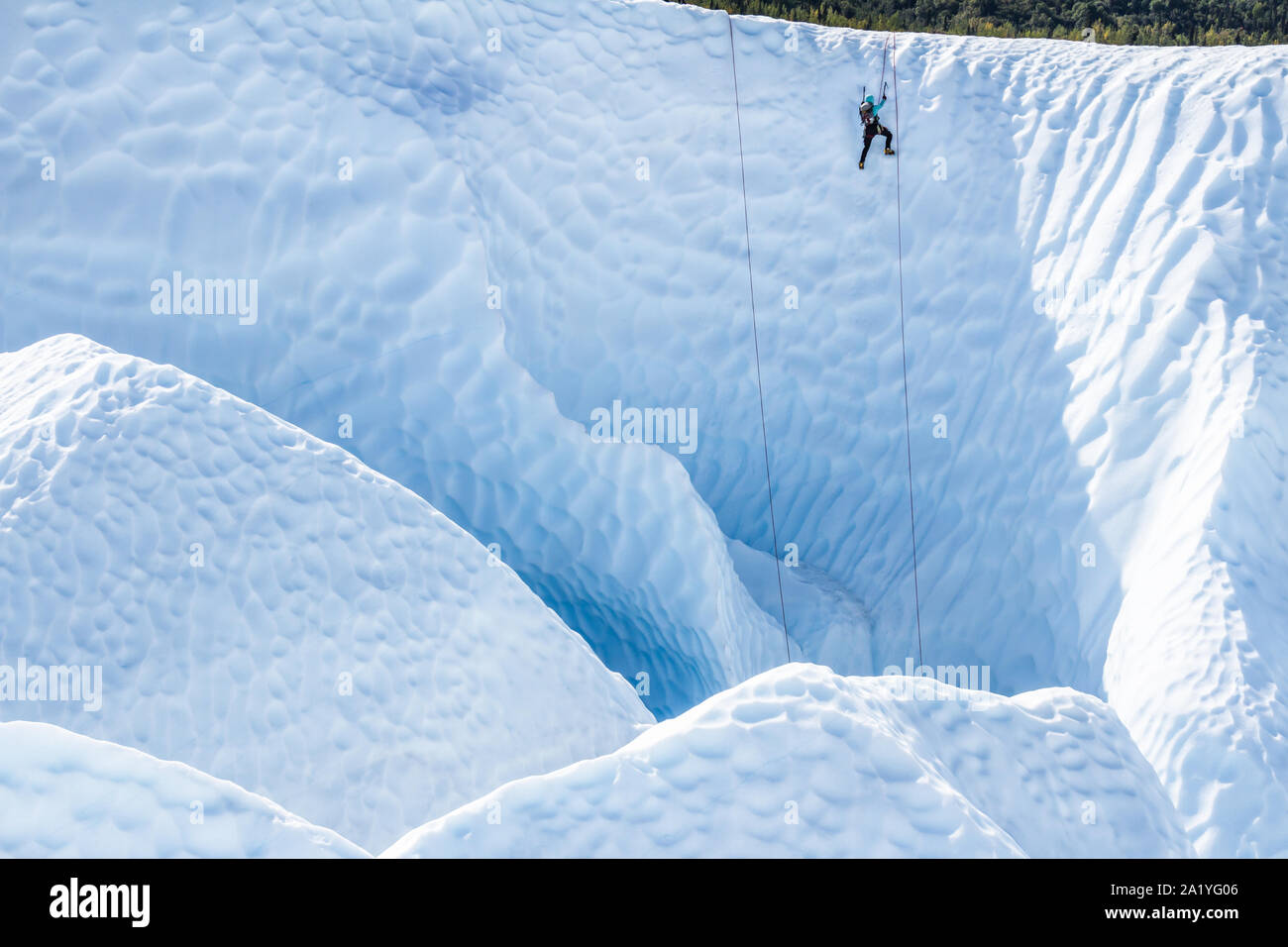 Auf der Matanuska Gletscher in Alaska, eine weibliche Gletscherführer Eis aus einem Canyon klettert Ihre Kunden oben zu unterstützen. Von einem anderen guide Absicherbare, mit ihr Stockfoto