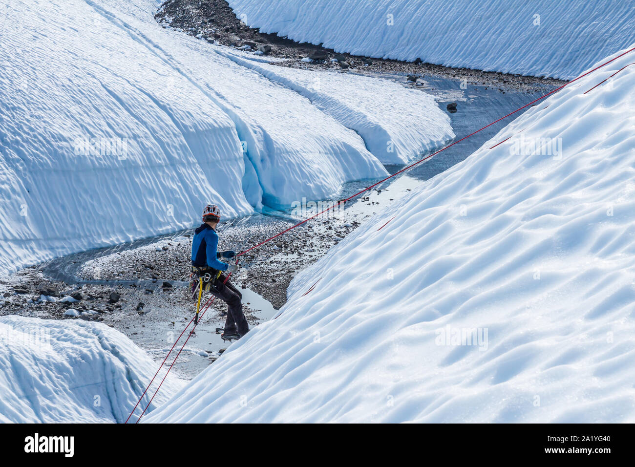 Ein junger Mann rappels oder Abseilstellen, unten ein Seil auf einer steilen Eis Hang auf der Matanuska Gletscher in Alaska. unter ihm ist eine große felsige Tal Schnitt in das wh Stockfoto