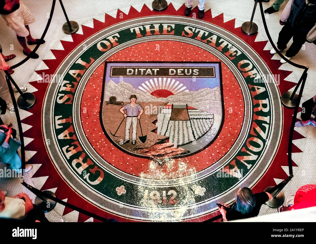 Dieser overhead View zeigt das große Siegel des Staates Arizona mit mulitcolored keramische Fliesen auf dem Boden der Rotunde im State Capitol Building in Phoenix, Arizona, USA erstellt. Es verfügt über Symbole der wichtigsten Unternehmen des Staates, die natürlichen Ressourcen und Attraktionen. Im Lieferumfang enthalten sind ein Gebirgszug mit der aufgehenden Sonne hinter den Gipfeln, ein Wasserreservoir und Dam, bewässerten Feldern und Obstplantagen und ein Quartz Mühle mit einem bergmann Holding ein Pick und Schaufel. Oberhalb dieser künstlerischen Darstellung ist das Motto, 'Ditat Deus", lateinisch für "Gott bereichert." Das Design dieser Dichtung Termine 1912 Stockfoto