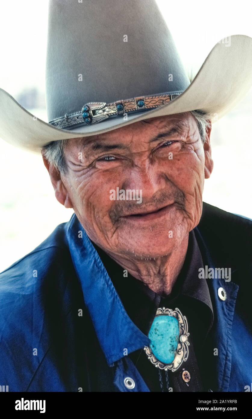Eine ältere Navajo Indianer lächelt unter seinen tall' zehn Gallonen Cowboy Hut für ein Portrait draußen im hellen Sonnenschein des südwestlichen Arizona, USA. Seine leder Hutband adjorned mit Silber und Türkis Perlen konkurriert für Aufmerksamkeit mit seinem Bolo Tie, verfügt über eine enorme türkis Edelstein von Silber von native Design umgeben. Viele der Navajo (manchmal buchstabiert Navaho), die indianischen Völker auch als Speisen bekannt, leben auf einem Vorbehalt, erstreckt sich über 14.000 Quadratkilometer meist trockenen Land in Arizona und New Mexico. Stockfoto