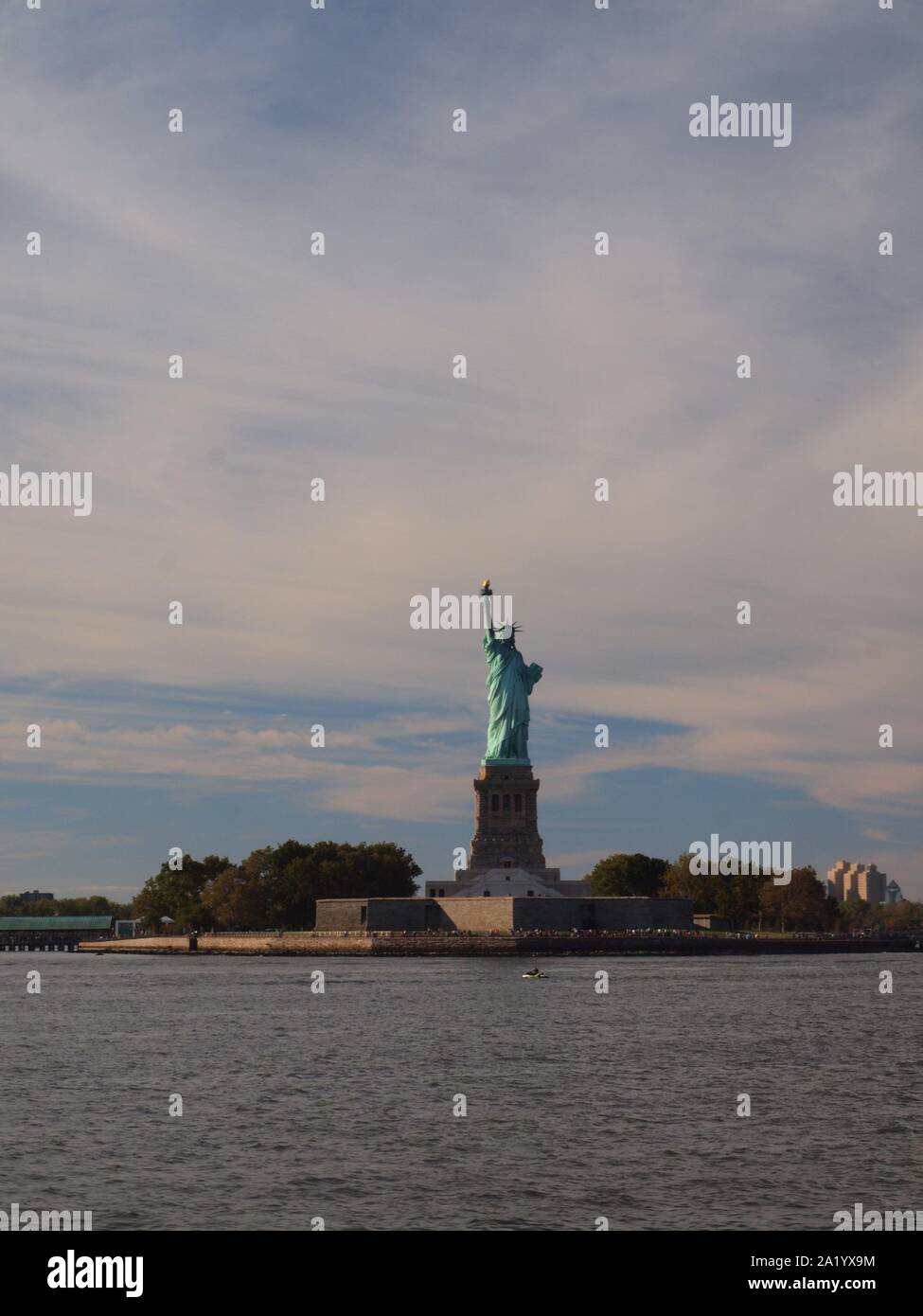 Beleuchtete Freiheitsstatue im Hafen von New York im September 2109. Ferner cargo Kräne am Hafen von Bayonne, NJ. Stockfoto