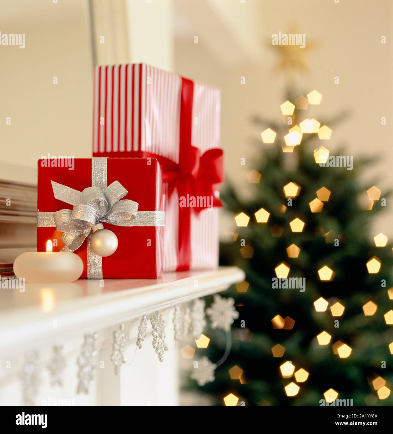 Lust auf Rot und Silber Weihnachten Geschenke Geschenke auf Wohnzimmer Mantel mit Kerze und geschmückten Baum im Hintergrund. Elegantes Ferienhaus Inneneinrichtung. Stockfoto