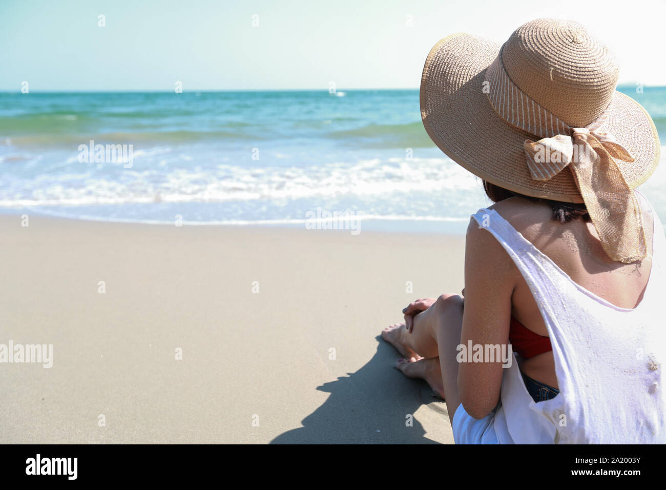 Rückansicht Portrait von sexy asiatische junge Mädchen im Bikini und Hut, weg zu tropischen Strand sitzend auf Sandstrand in der Natur mit blauen Himmel. Stockfoto