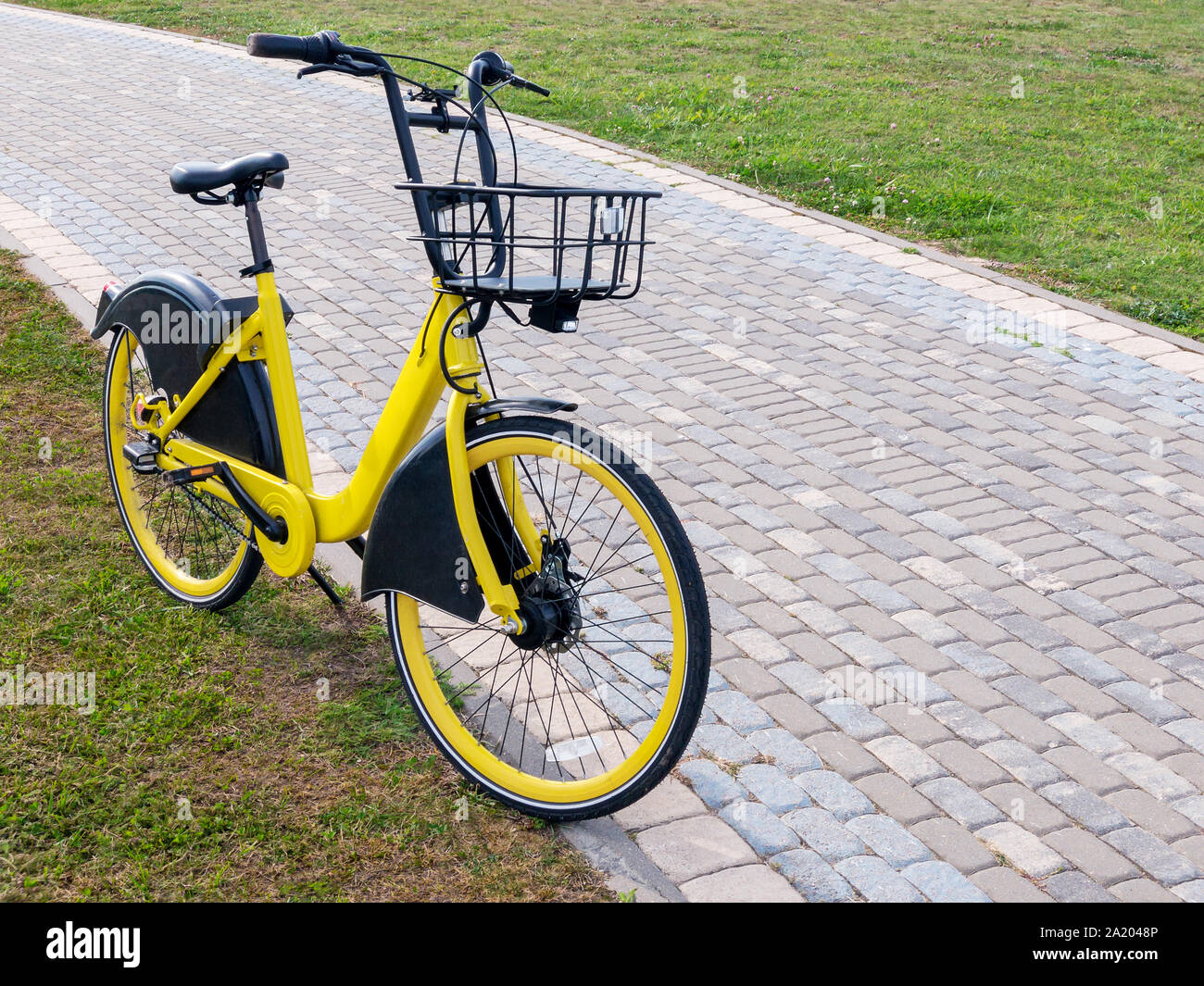 Yellow Bike mit Essen Korb stehend auf grünem Gras in der Nähe von Fußweg. Stadt Fahrräder zu mieten Stockfoto