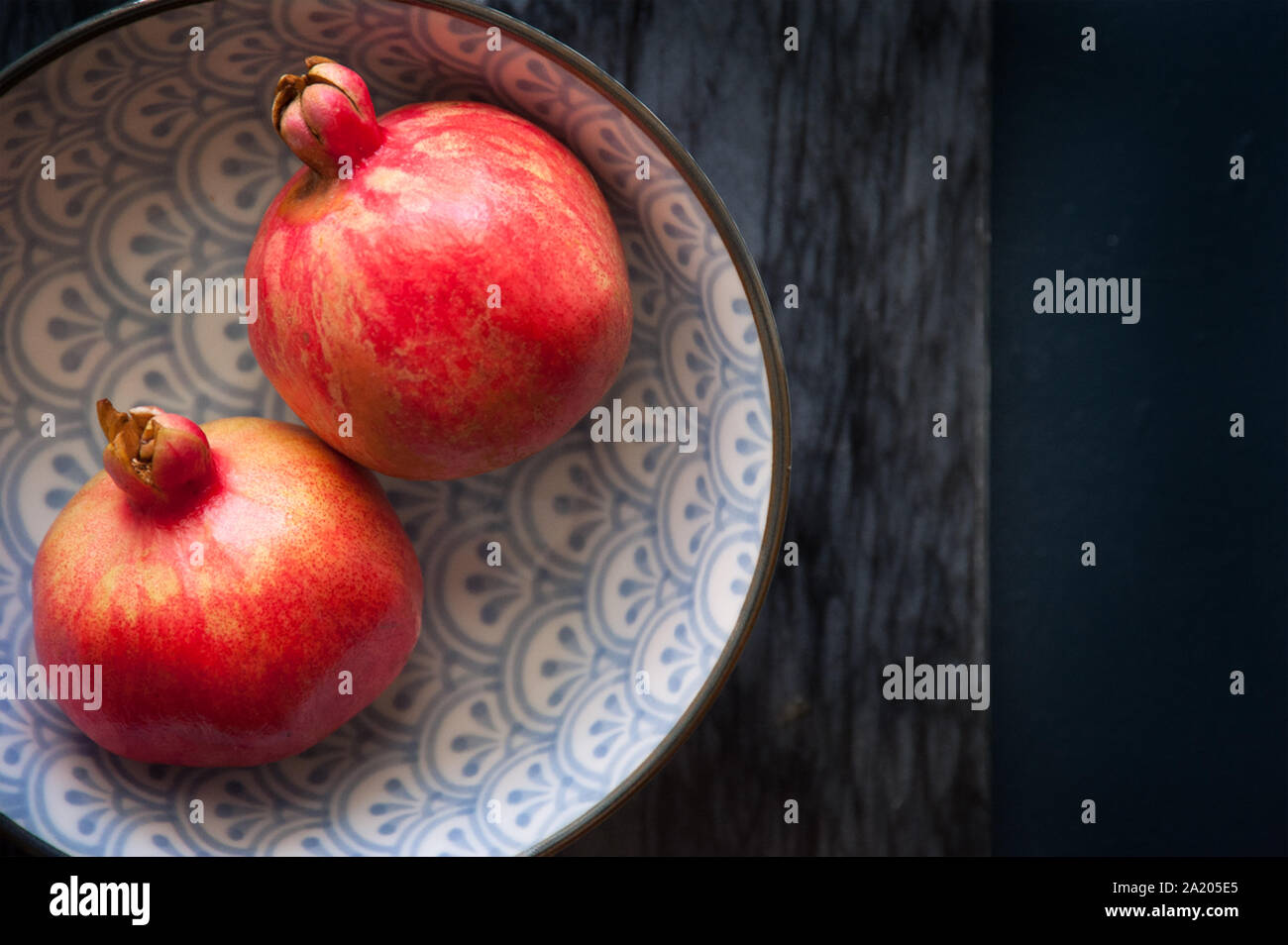 Flachbild - Fotografie von 2 Granatäpfel in einer gemusterten blaue Schale auf einem Marmorboden und dunklen blauen Hintergrund. Stockfoto