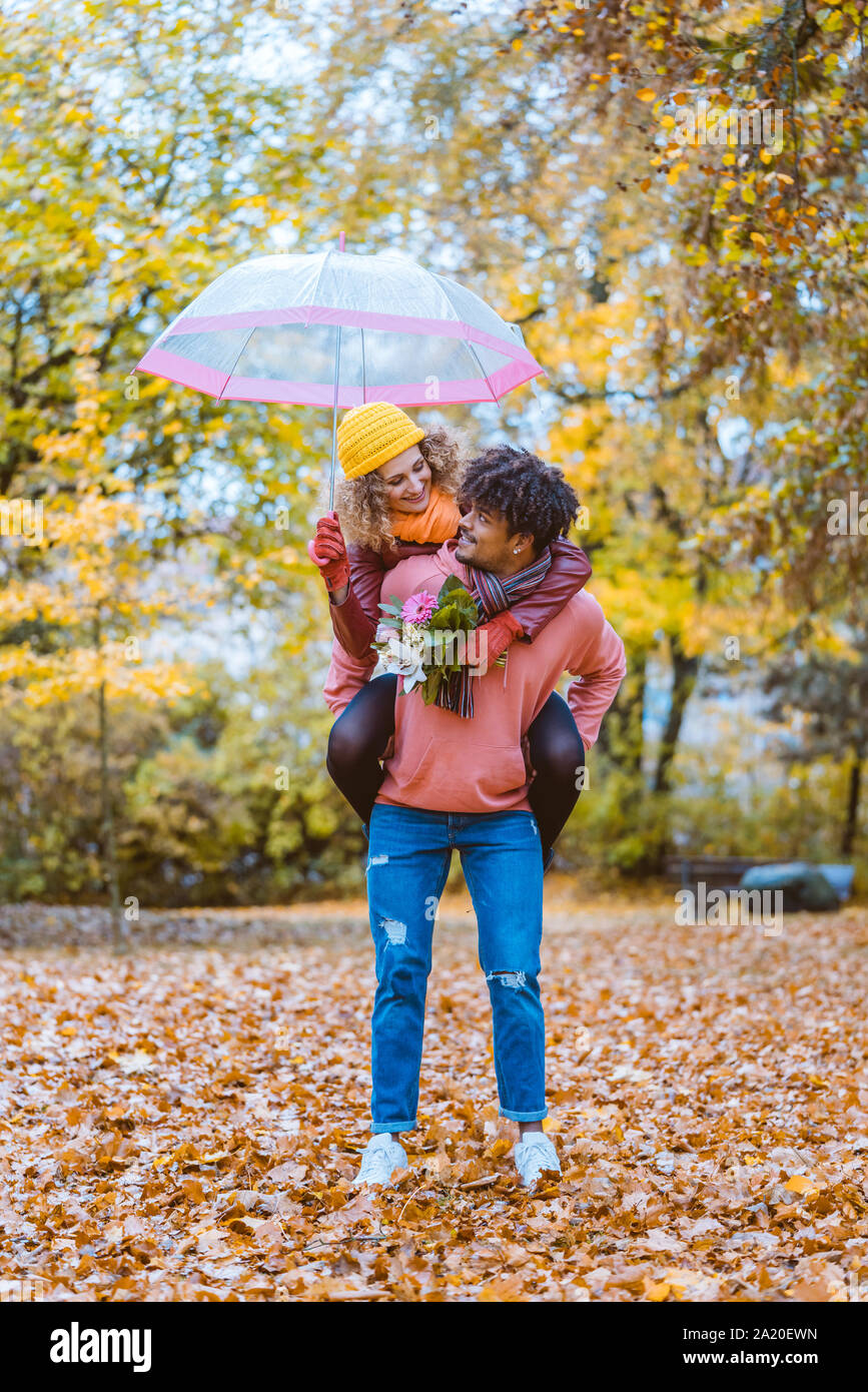 Schwarzer Mann, der seine kaukasische Mädchen huckepack im Herbst Stockfoto