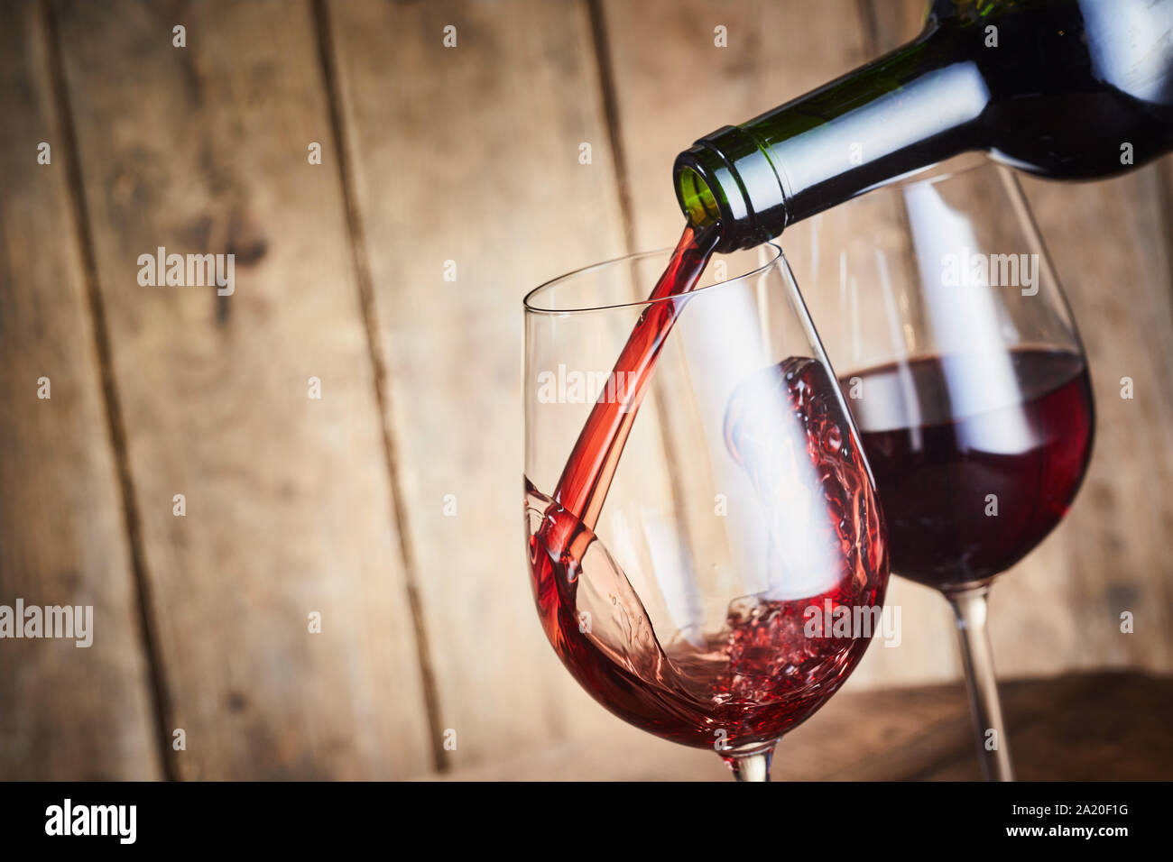 Ein Glas trockener Rotwein aus der Flasche ausgegossen werden in stilvolle Weingläser über rustikale Holz mit Kopie Raum Stockfotografie