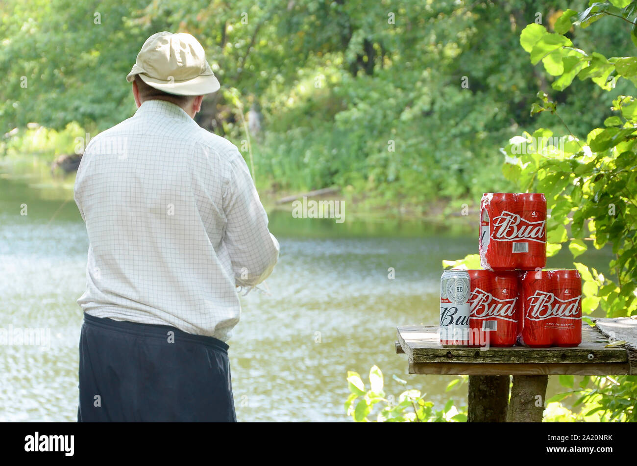 Kharkov, Ukraine - August 10, 2019: Budweiser Bud Bierdosen pack auf alten Tisch und Fischer am Fluss für den Hintergrund. Budweiser ist einer der beliebtesten Stockfoto