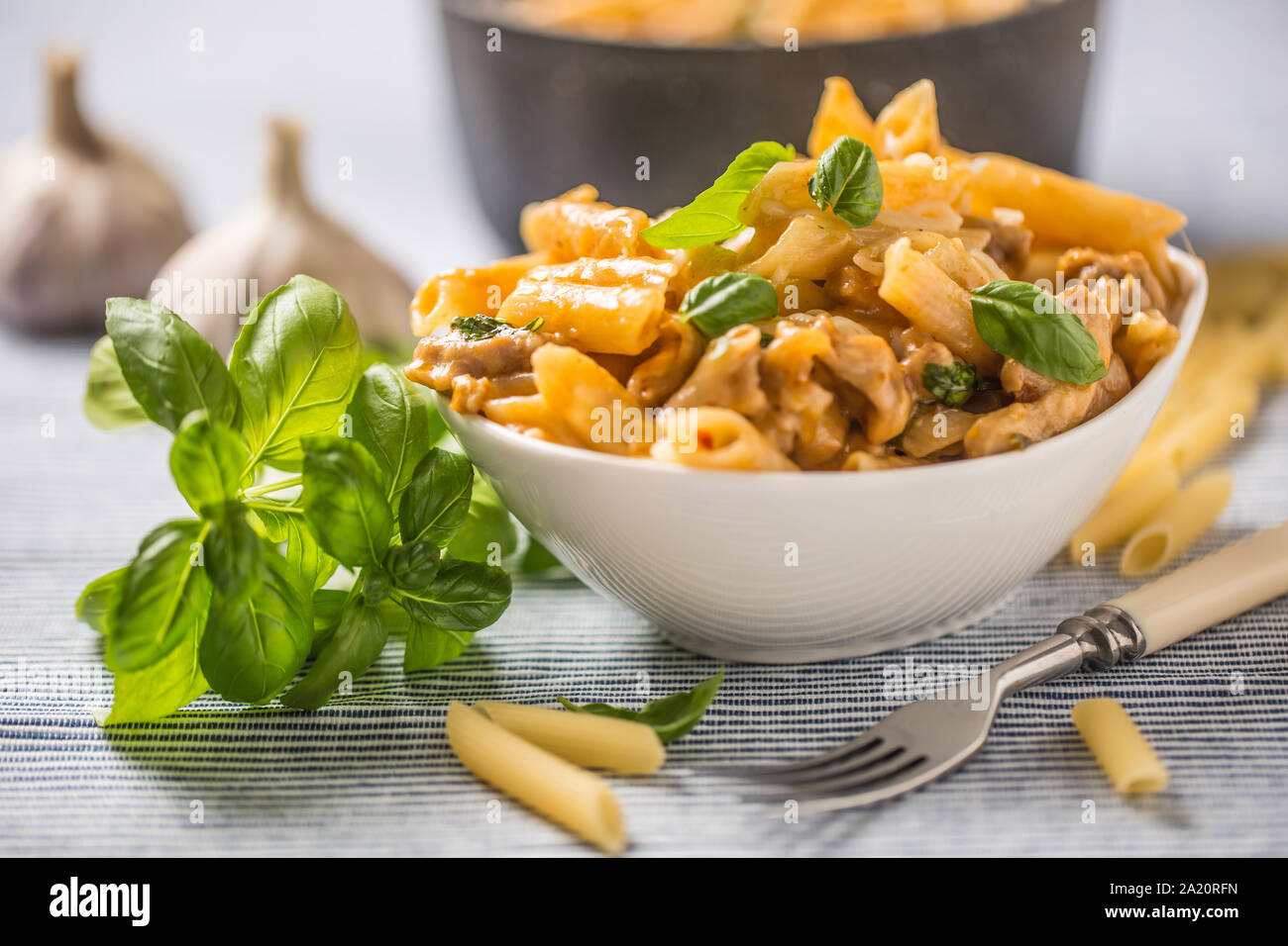 Pasta Penne mit Huhn Stücke Pilze Basilikum und Parmesan italienische Küche in weiße Schüssel am Küchentisch Stockfoto