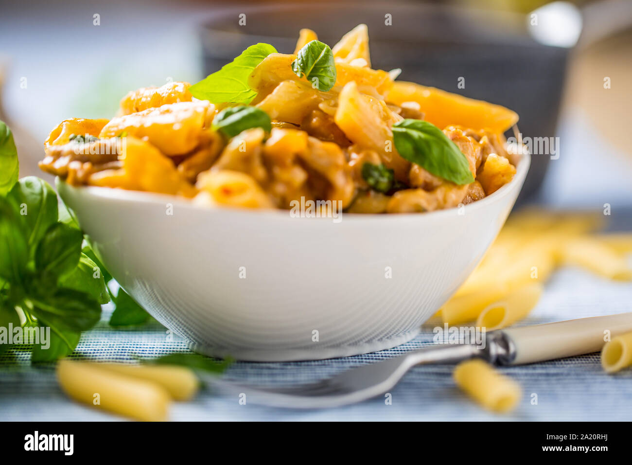 Pasta Penne mit Huhn Stücke Pilze Basilikum und Parmesan italienische Küche in weiße Schüssel am Küchentisch Stockfoto