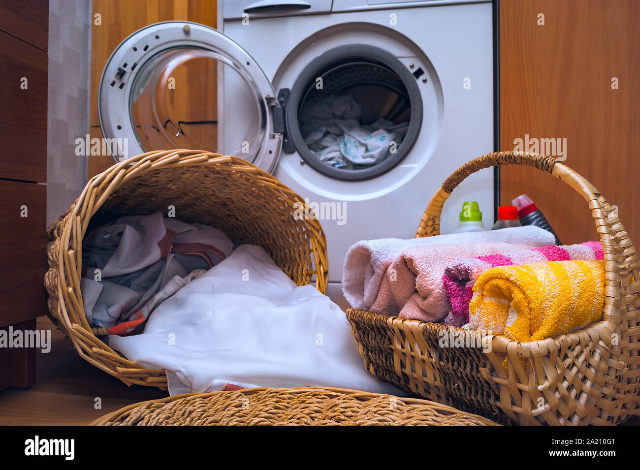 Saubere Handtücher, schmutzige Wäsche in der korbwaren Wäschekörbe,  flüssige Waschmittel auf dem Boden in der Nähe der vorderen Last  Waschmaschine mit geöffneter Tür. Haus Interi Stockfotografie - Alamy