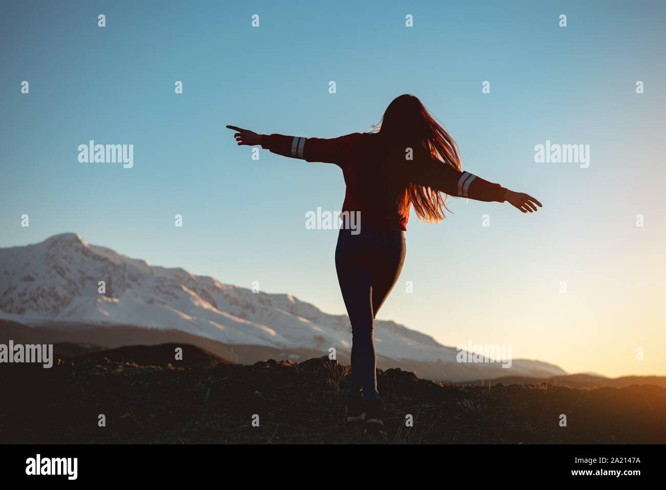 Schöne schlanke Mädchen geht mit erhobenen Armen gegen Sonnenuntergang Berge und Himmel Stockfoto