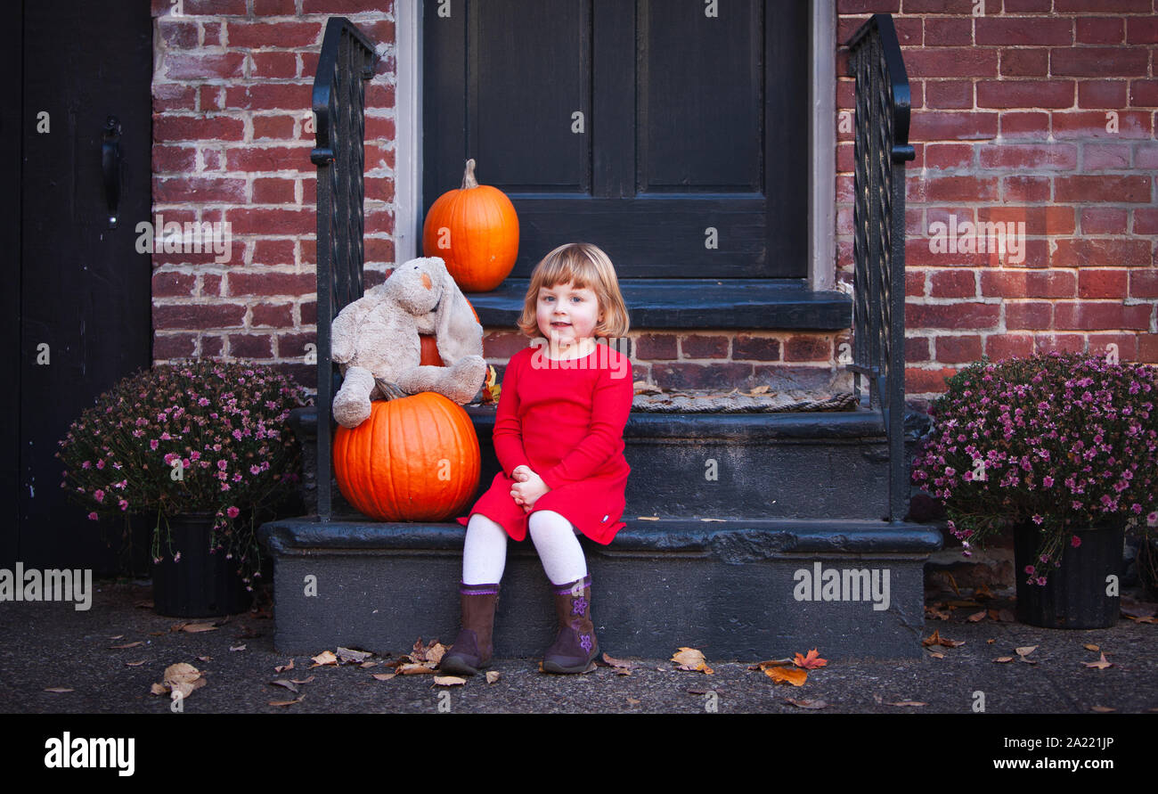 Kleines Mädchen sitzt auf der Haustür durch orange Kürbisse in Old Town Alexandria, Virginia Umgeben Stockfoto