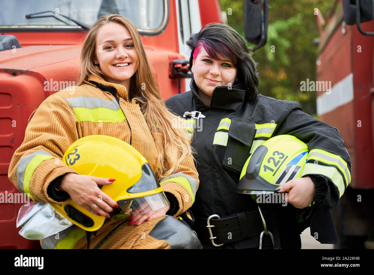 Bild von zwei Frauen Feuerwehrmann mit Helm in der Hand neben Feuerwehr Auto auf der Straße Stockfoto