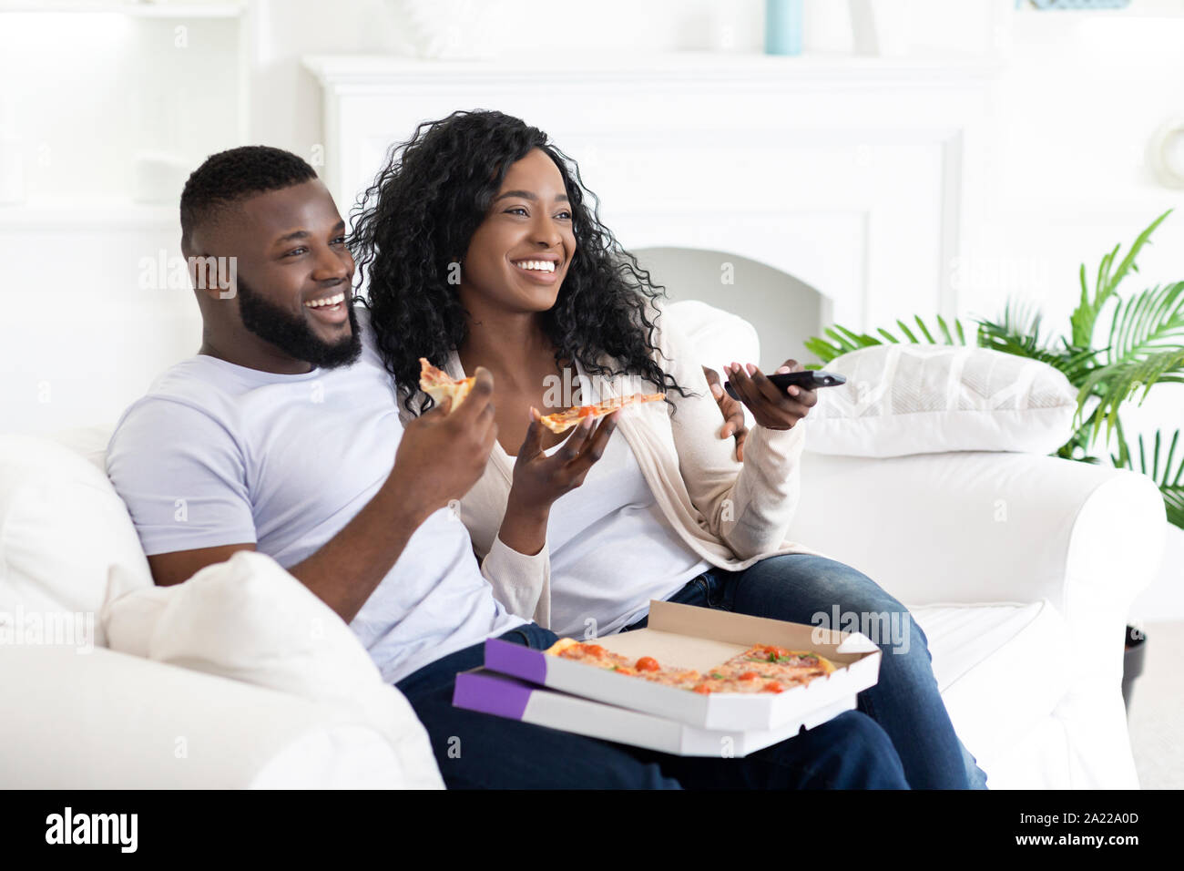 Gerne afrikanische amerikanische Paar essen Pizza zu Hause auf der Couch sitzen und Fernsehen Stockfoto