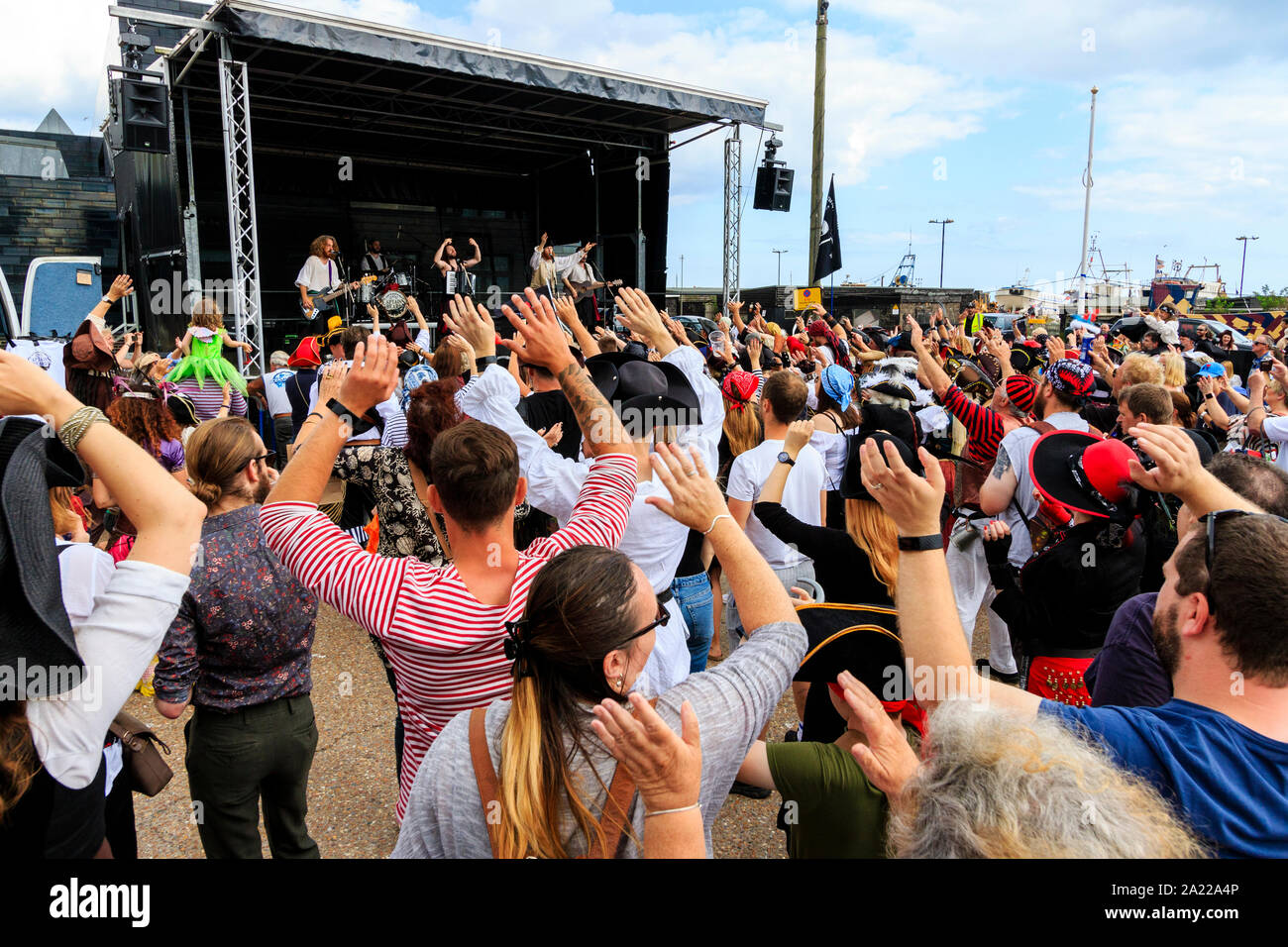 Ansicht von hinter dem Publikum ihre Armen, während Band, Kapitäne Bart, führt auf der Bühne an der Piraten Tag in Hastings. Tagsüber, blauer Himmel. Stockfoto