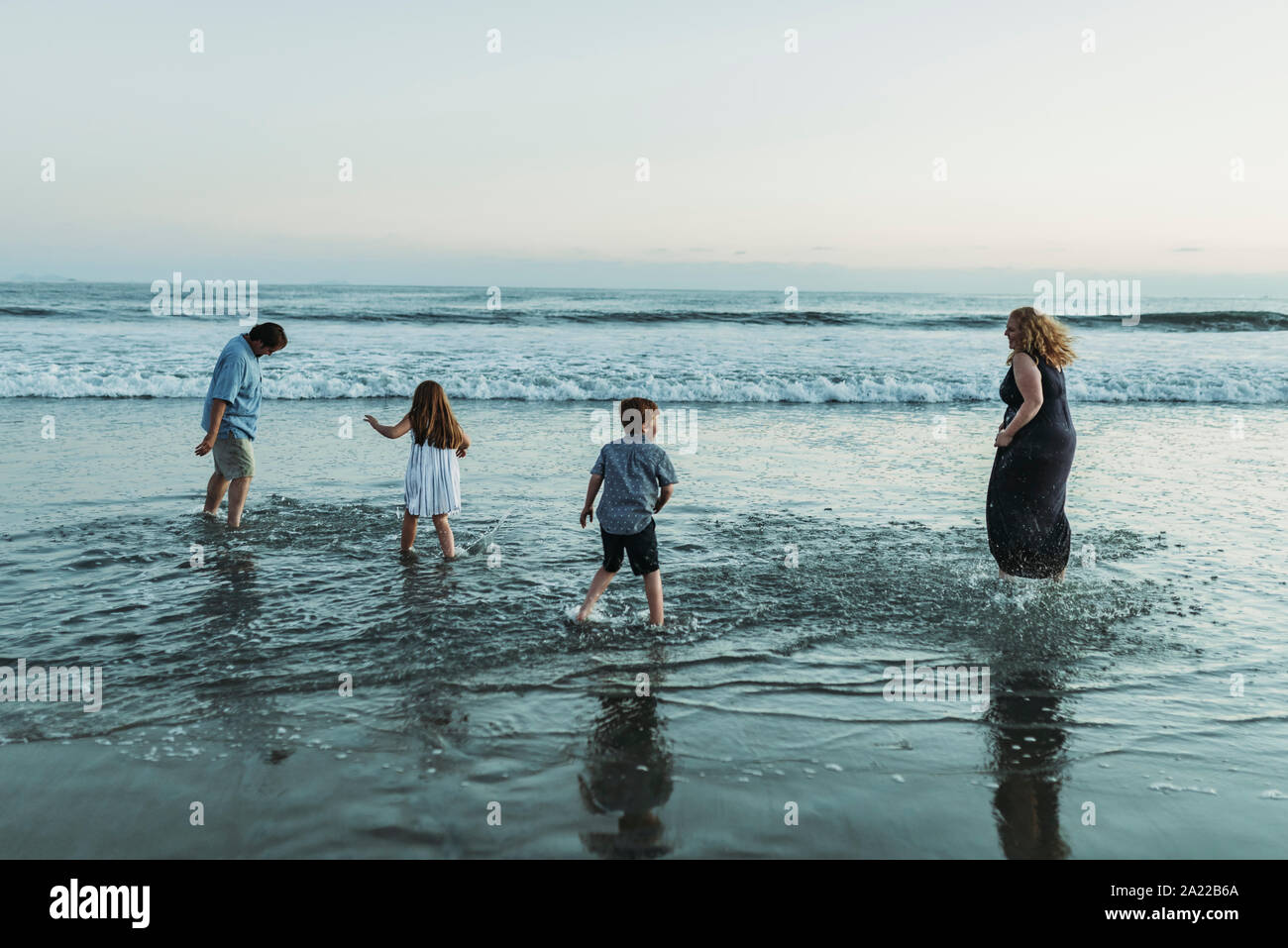 Familie von vier Spielen und Plantschen im Meer in der Dämmerung Stockfoto