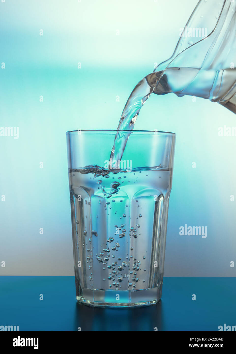 Wasser mit Luftblasen im Glas. Gießen Sie Wasser aus einem Krug in ein Glas. Licht durch ein Glas. Kreative Zusammenfassung Hintergrund. Stockfoto