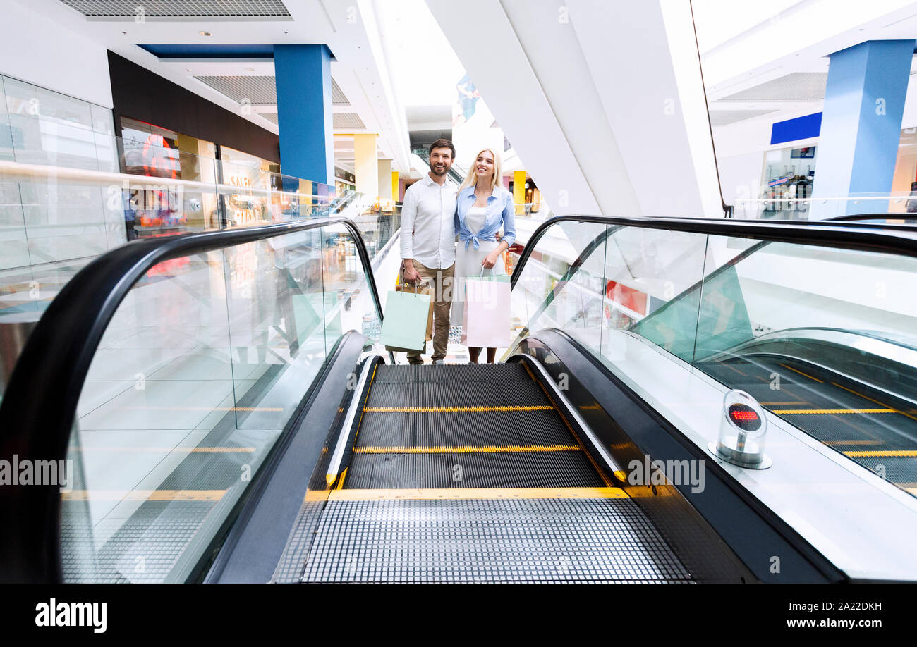 Zusammen einkaufen. Freundliche Paar ständigen Umarmen auf Rolltreppe Holding Shopper Taschen in der Mall. Leerer Raum, selektiven Fokus Stockfoto