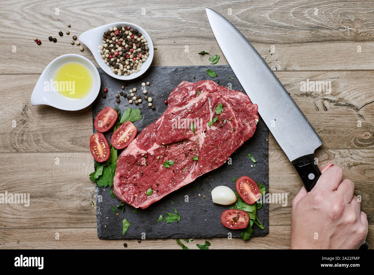Weibliche Hand bereitet Essen, ein rohes Rib-Eye Steak mit frischen Gewürzen auf einem Schiefertafel und Holztisch. Stockfoto