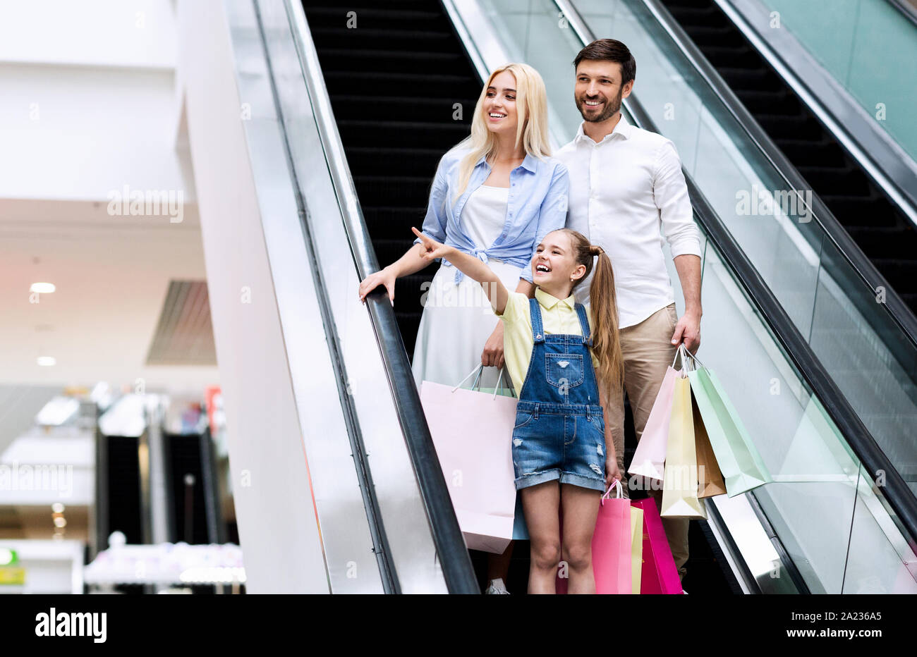 Familie Shopping Konzept. Tochter Zeigefinger auf der Rolltreppe, Eltern zu etwas In Mall kaufen. Freier Speicherplatz Stockfoto
