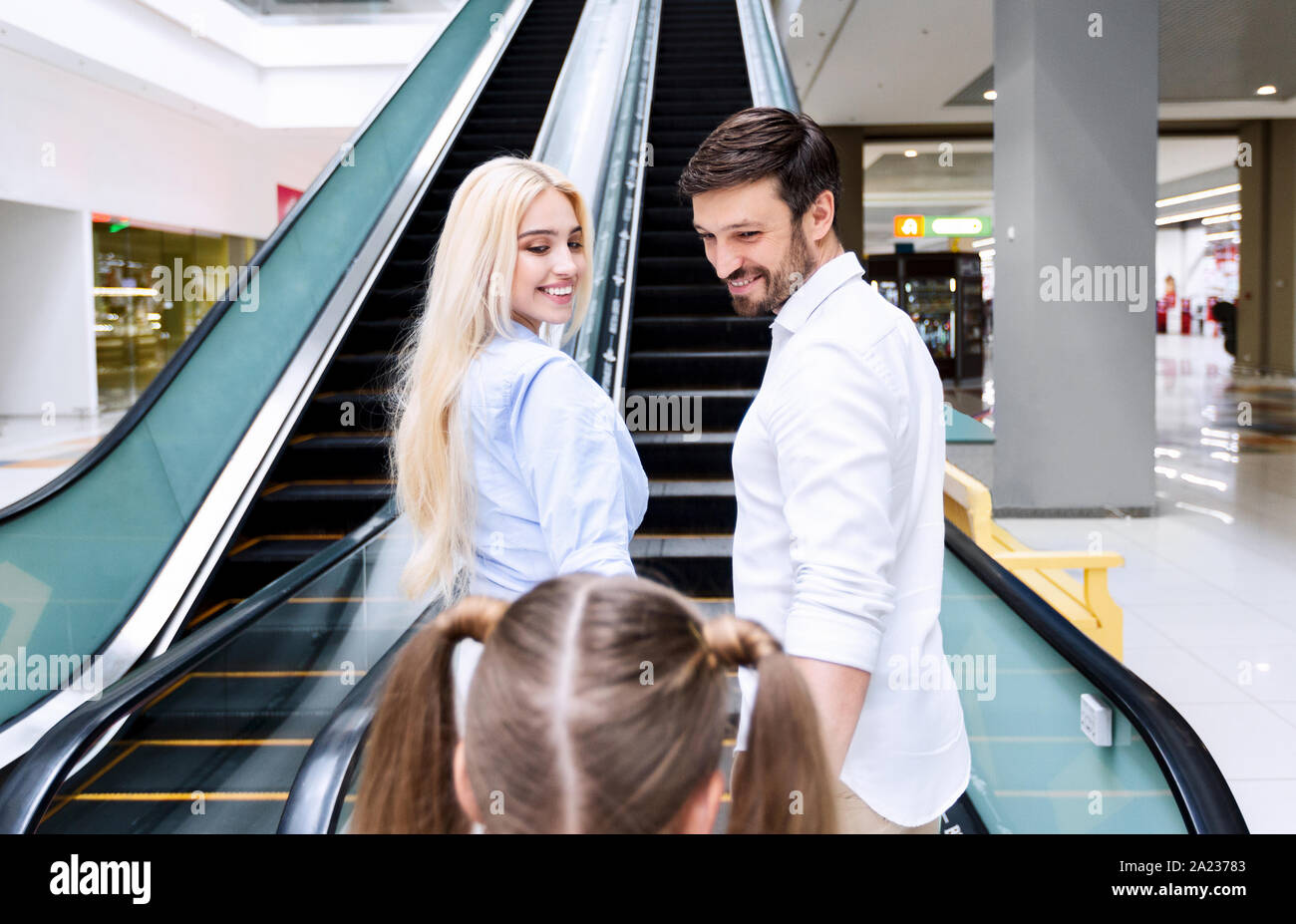 Positive Eltern und Tochter stehen auf Rolltreppe in Einkaufszentrum Förderung Ihr auf Rolltreppen zu erhalten. Escalaphobia Stockfoto