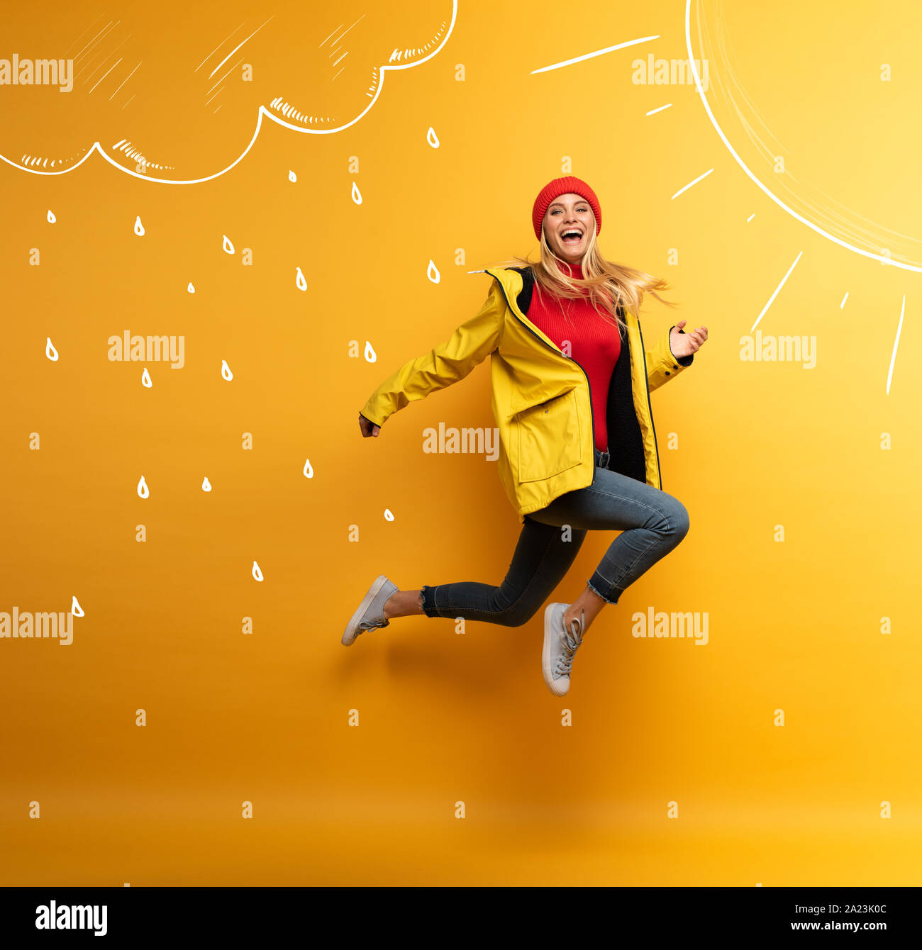 Mädchen mit Jacke springt auf die Sonne aus dem regnerischen Wetter. Freudige Ausdruck. Gelber Hintergrund Stockfoto