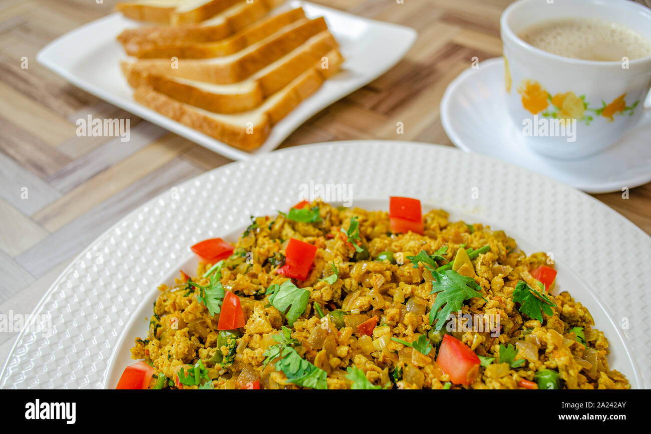 Ei Bhurji mit Korianderblättern und Kokosnuss zusammen mit Brot und Tee. Nahaufnahme von einem typischen indischen Frühstück. Stockfoto
