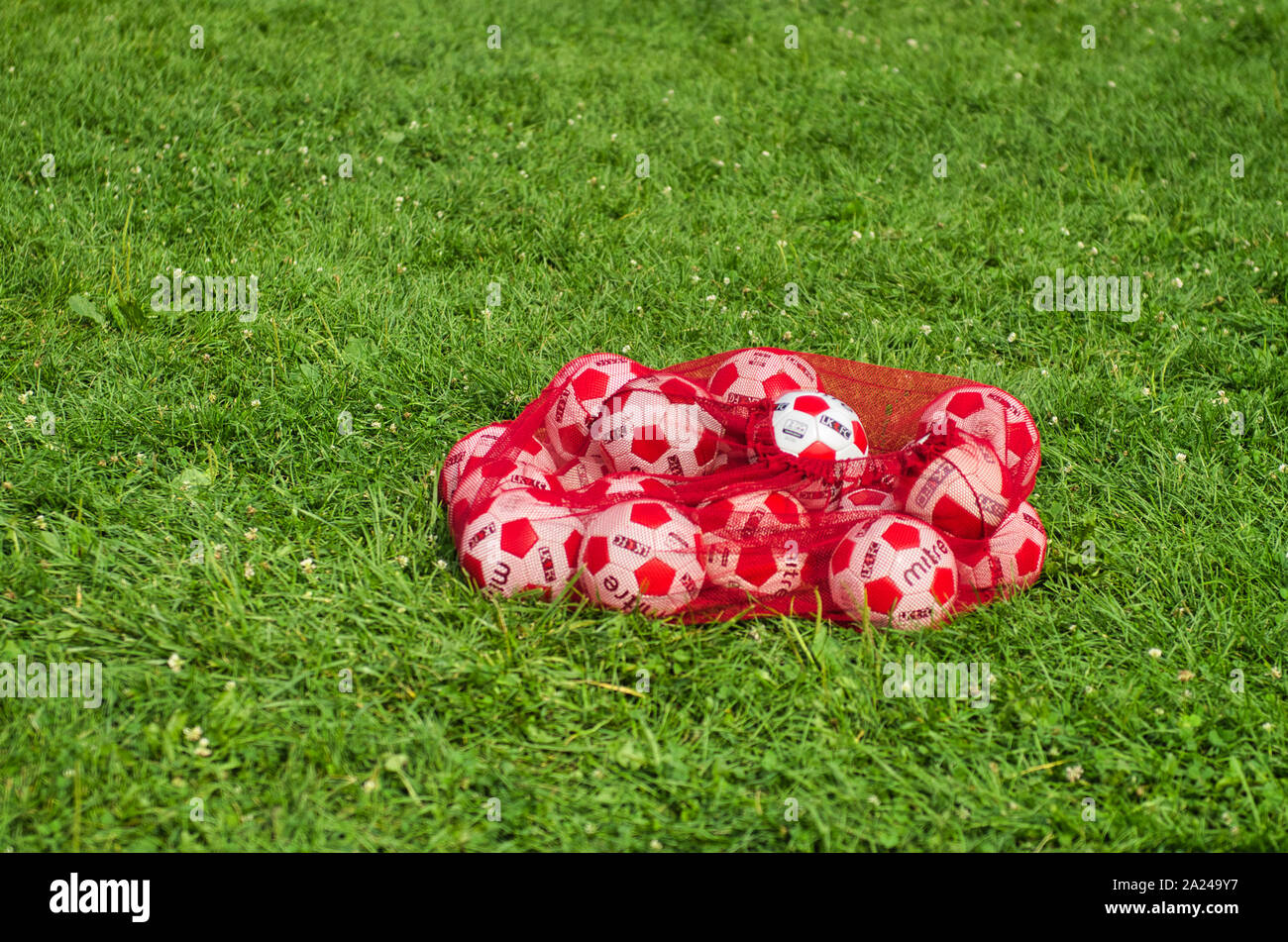 Eine rote Tasche von weißen und roten Fußball Bälle auf dem grünen Rasen auf dem Fußballplatz während kinder fussball Klasse Stockfoto