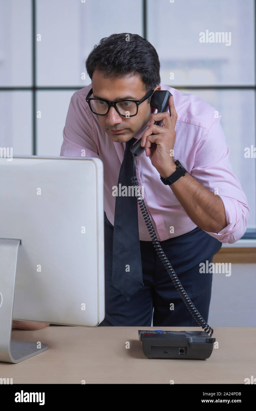 Geschäftsmann in Brillen sprechen über Telefon an den Computer in der Nähe von seinem Schreibtisch im Büro suchen Stockfoto