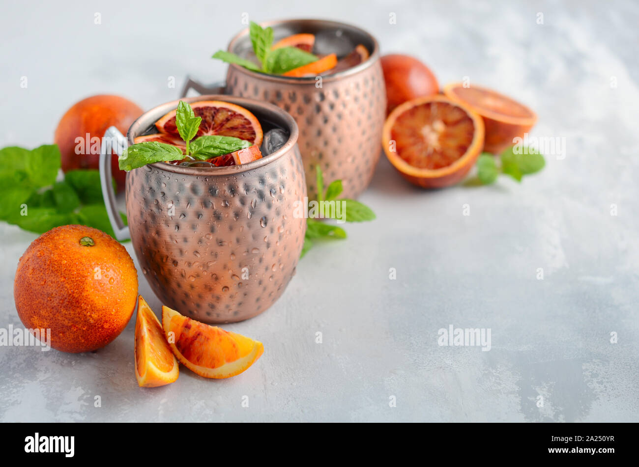 Blutorange Moscow Mule Alkohol Cocktail mit frischen Minzeblättchen und Eis in Kupfer Tassen auf grauem Beton Hintergrund. Stockfoto