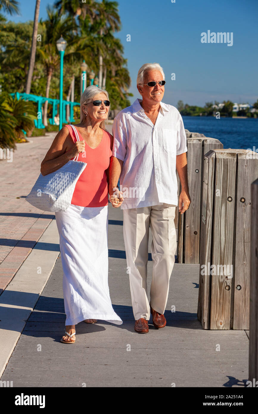 Gerne älterer Mann und Frau romantische Paar zusammen halten sich an den Händen und heraus zum tropischen Meer oder Fluss mit hellen blauen Himmel suchen Stockfoto