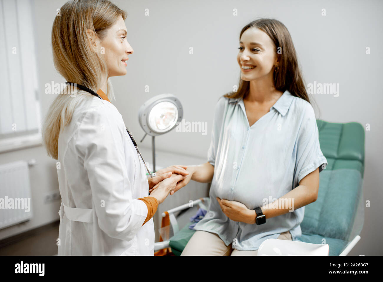 Junge schwangere Frau sitzt auf dem gynäkologischen Stuhl während einer medizinischen Beratung