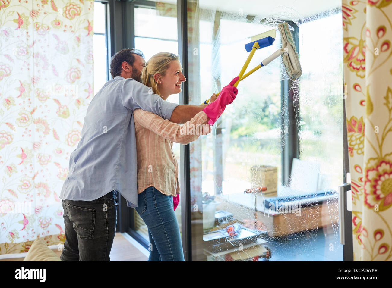 Glückliches junges paar Reinigung der Fenster im Wohnzimmer beim Frühjahrsputz Stockfoto