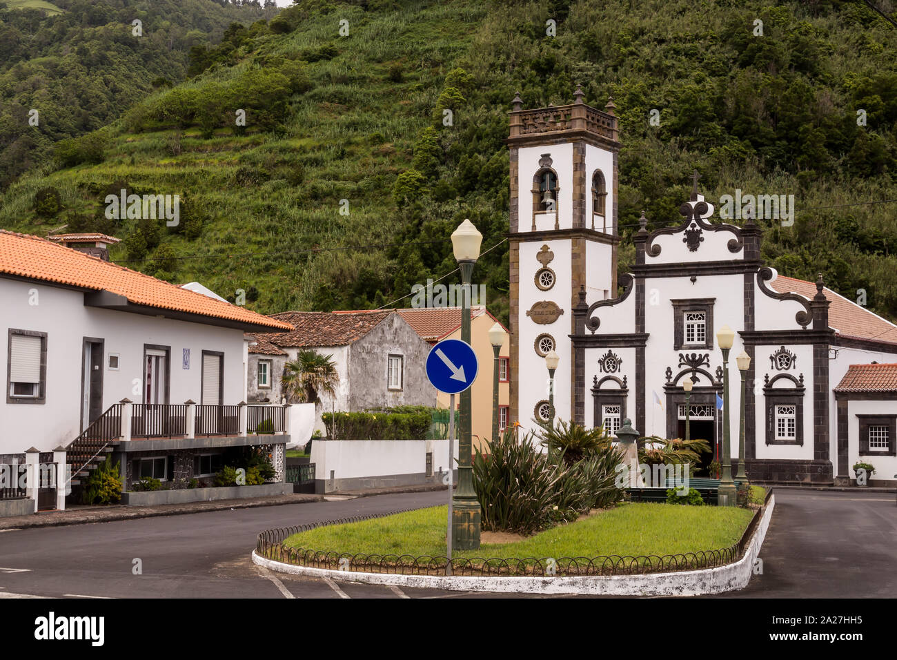Platz geteilt durch Gras Insel mit einem Verkehrsschild, von Häusern umgeben. Typisch portugiesische weißen Kirche. Wald auf einem Hügel im Hintergrund. Faial d Stockfoto