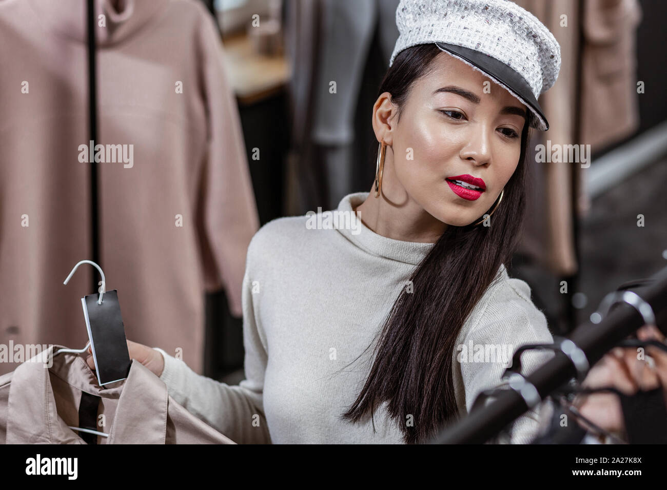 Schöne junge Dame an Labels von trenchcoats im Shop suchen Stockfoto
