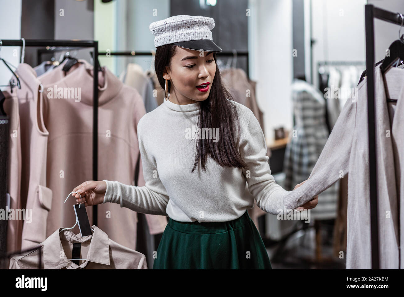Gut aussehende junge Frau berühren verschiedene Trenchcoats im Fashion Store Stockfoto