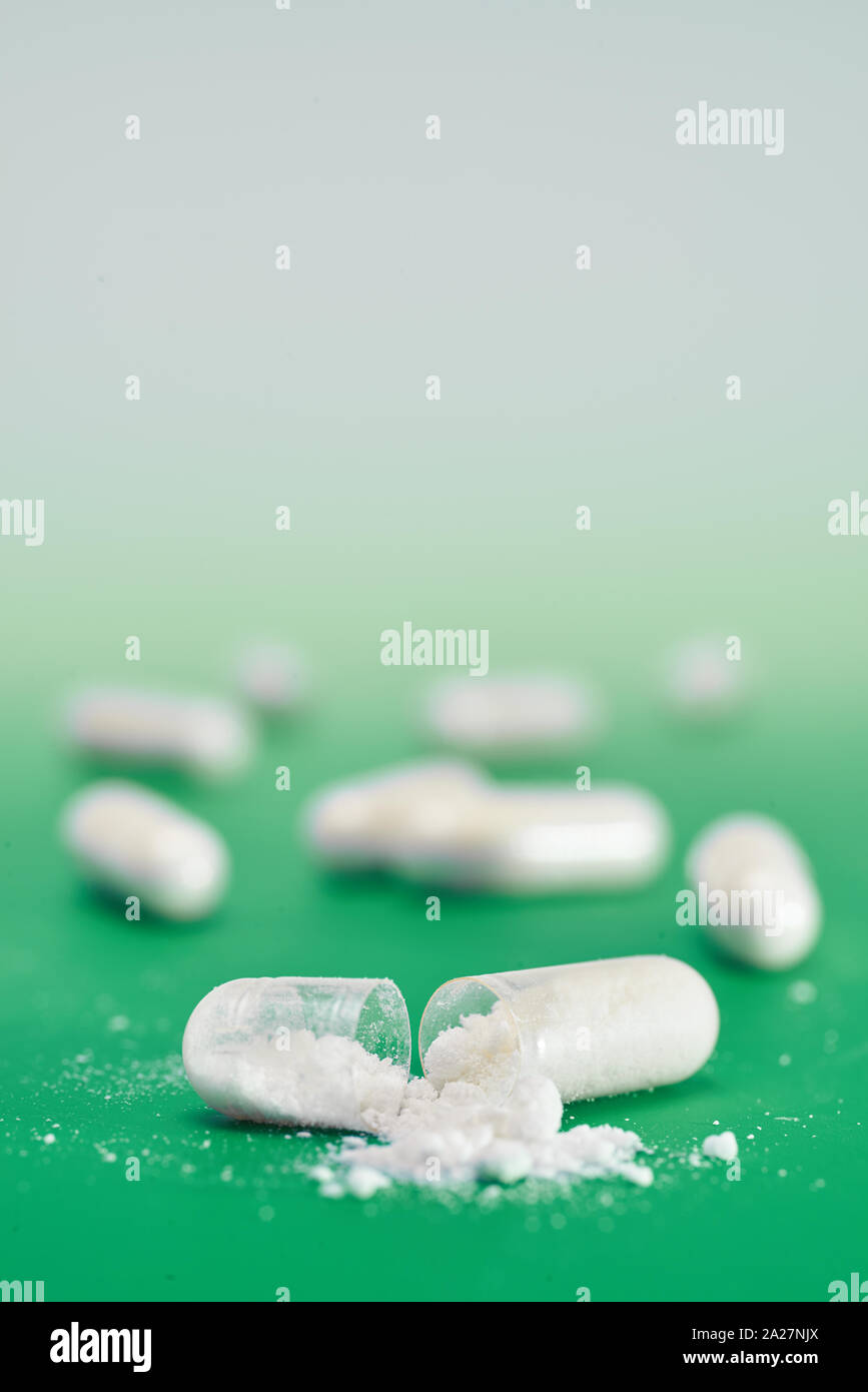 Nahaufnahme auf weiße Kapsel mit weißen Medikation Pulver Split geöffnet auf grüne Minze Hintergrund, vertikale Komposition mit copy-Raum Stockfoto